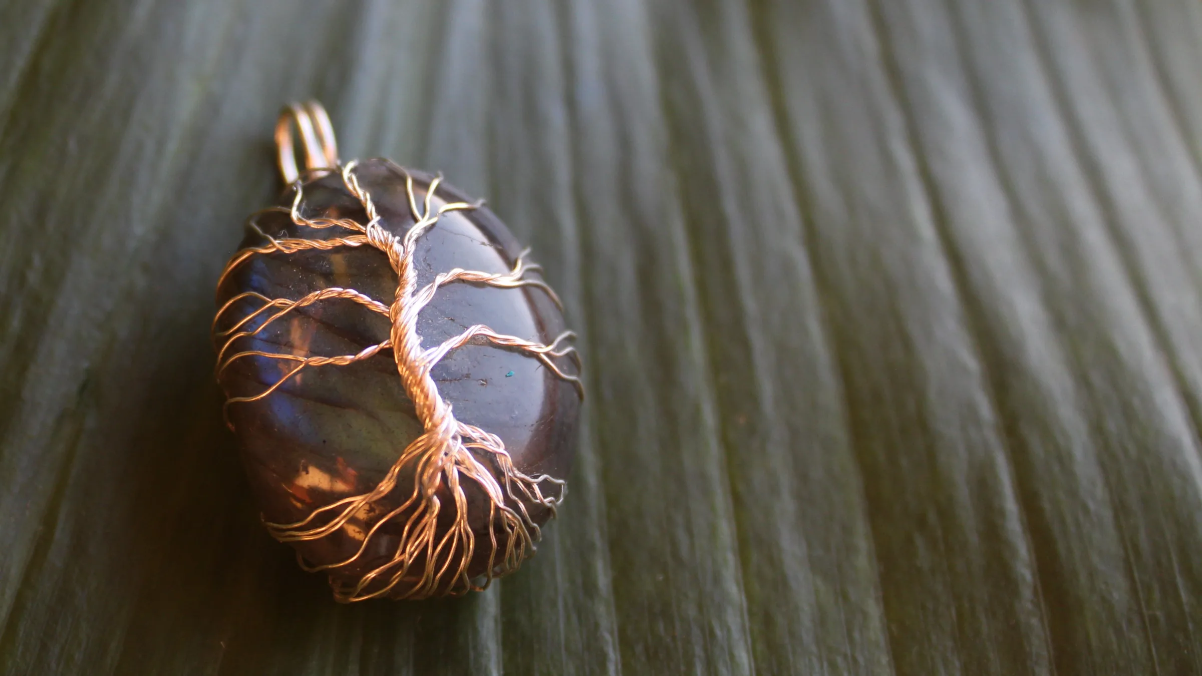 Copper tree of life pendant on a labradorite stone, lying on a green leaf